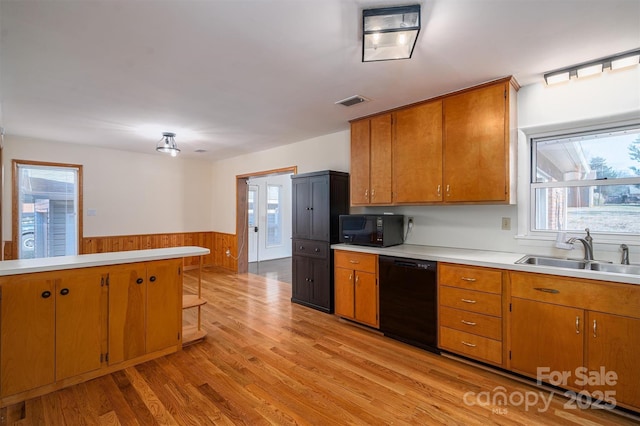 kitchen featuring brown cabinetry, a wainscoted wall, light countertops, black appliances, and a sink