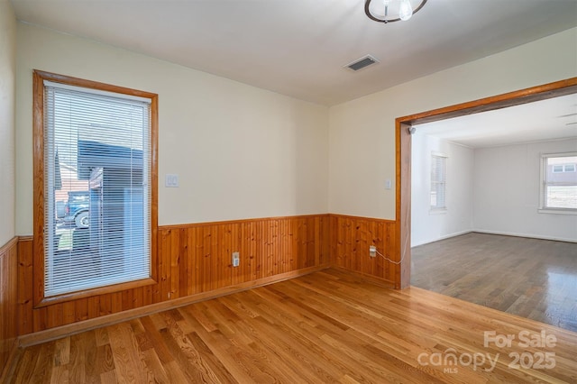 spare room with wainscoting, visible vents, and wood finished floors