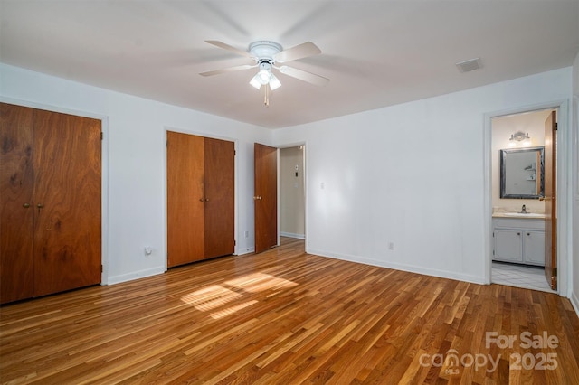 unfurnished bedroom featuring light wood finished floors, two closets, visible vents, a sink, and baseboards