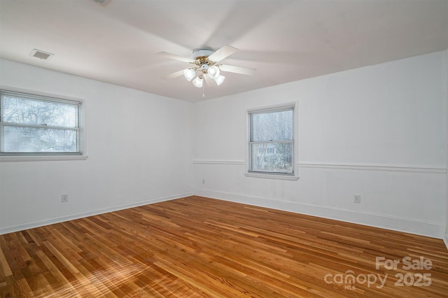 unfurnished room with baseboards, visible vents, a ceiling fan, and wood finished floors