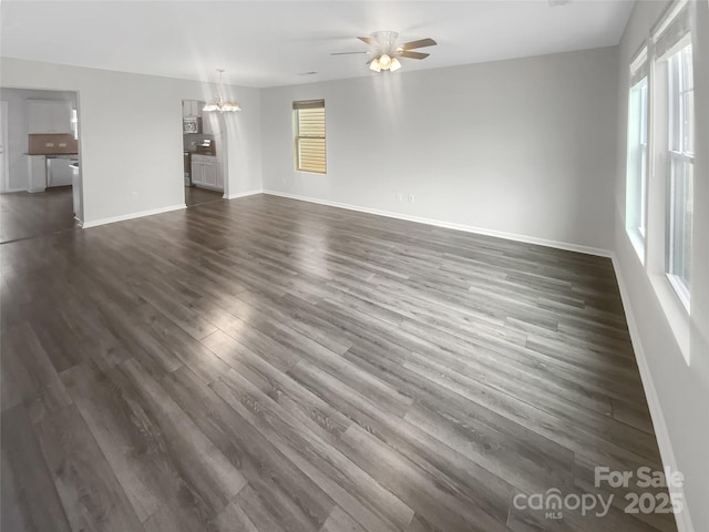 unfurnished living room with baseboards, dark wood finished floors, and ceiling fan with notable chandelier