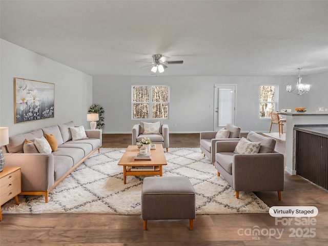 living area with ceiling fan with notable chandelier, wood finished floors, and baseboards