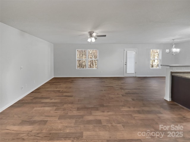 unfurnished living room with dark wood-style floors, baseboards, and ceiling fan with notable chandelier