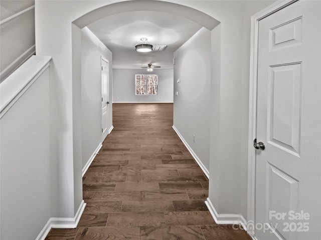 hall with dark wood-type flooring, arched walkways, visible vents, and baseboards