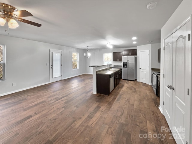 kitchen featuring a kitchen island with sink, stainless steel appliances, a sink, open floor plan, and dark wood-style floors