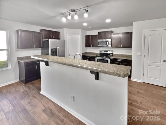 kitchen featuring stainless steel appliances, wood finished floors, baseboards, dark brown cabinets, and a kitchen bar