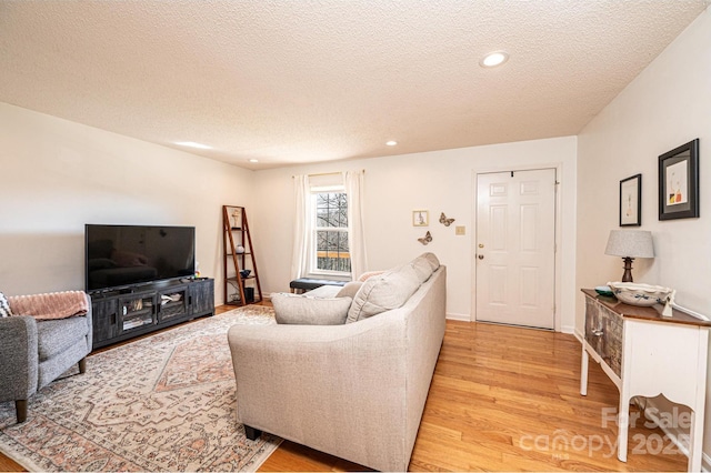 living room with light wood-type flooring, a textured ceiling, baseboards, and recessed lighting