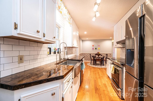 kitchen with a textured ceiling, stainless steel appliances, a sink, white cabinetry, and light wood-style floors