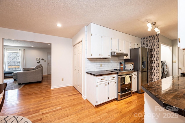 kitchen with white cabinets, dark countertops, appliances with stainless steel finishes, open floor plan, and under cabinet range hood