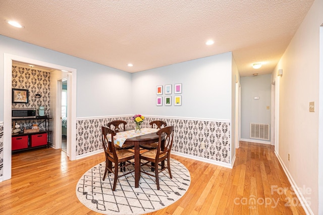 dining room with hardwood / wood-style flooring, visible vents, a textured ceiling, and wallpapered walls