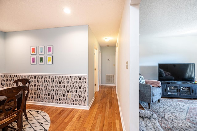 hallway with light wood-style floors, visible vents, a textured ceiling, and baseboards