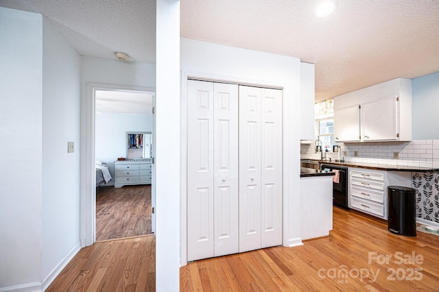 kitchen featuring tasteful backsplash, white cabinetry, a sink, and light wood finished floors