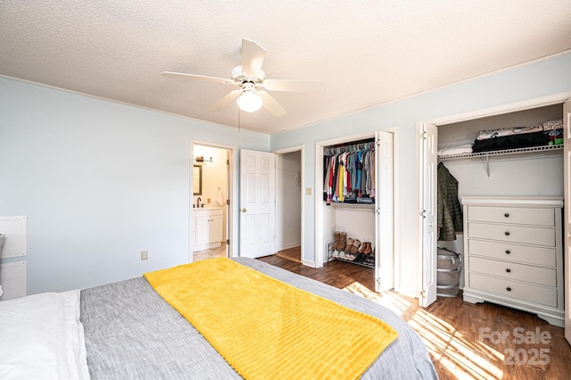 bedroom with a textured ceiling, ensuite bathroom, dark wood-style flooring, a ceiling fan, and two closets