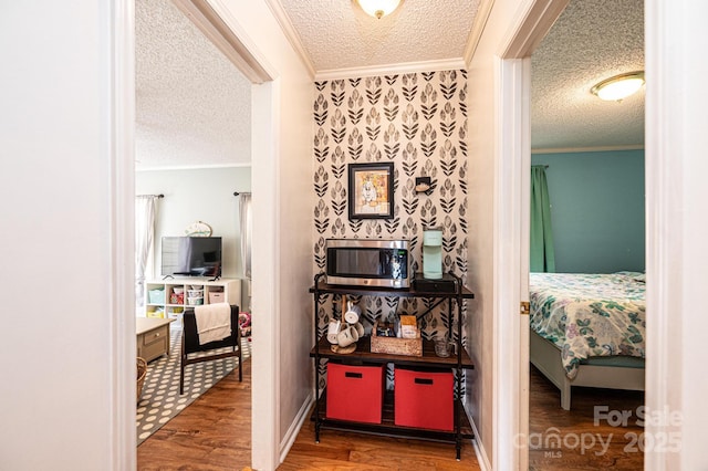 hallway with a textured ceiling, ornamental molding, and wood finished floors