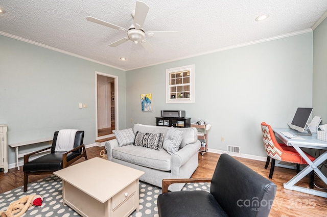 living room with visible vents, light wood-style floors, ornamental molding, a ceiling fan, and baseboards