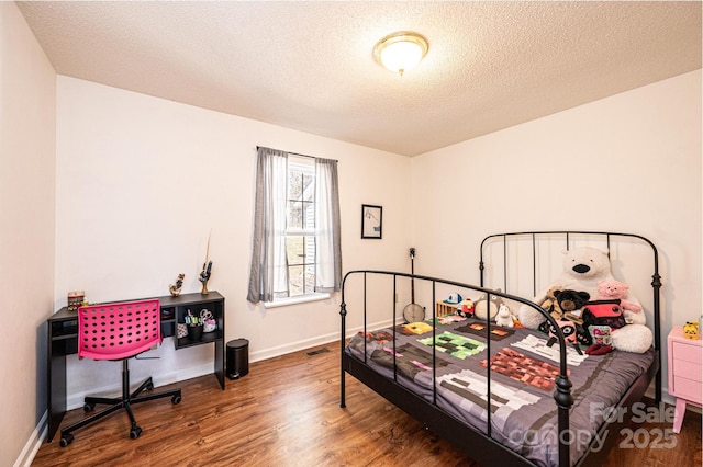 bedroom with visible vents, a textured ceiling, baseboards, and wood finished floors