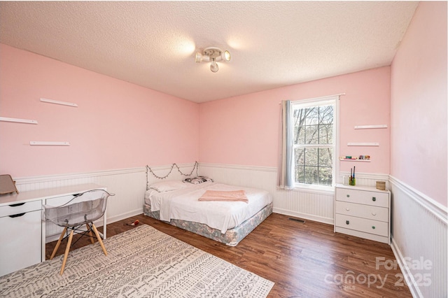 bedroom featuring visible vents, a wainscoted wall, a textured ceiling, and wood finished floors