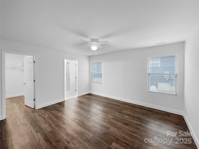 unfurnished bedroom with a closet, a spacious closet, ceiling fan, wood finished floors, and baseboards