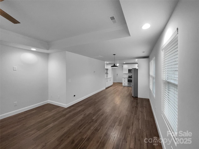 unfurnished living room featuring recessed lighting, dark wood-style flooring, visible vents, baseboards, and a raised ceiling