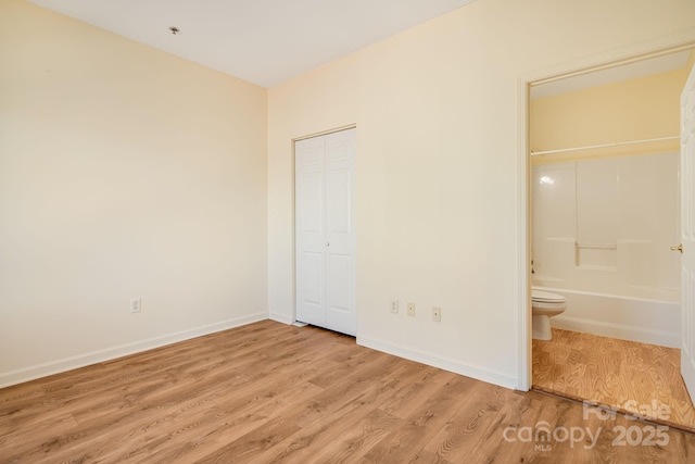 unfurnished bedroom with light wood finished floors, baseboards, a closet, and ensuite bathroom