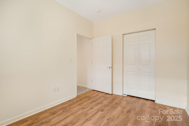 unfurnished bedroom featuring light wood finished floors, a closet, and baseboards