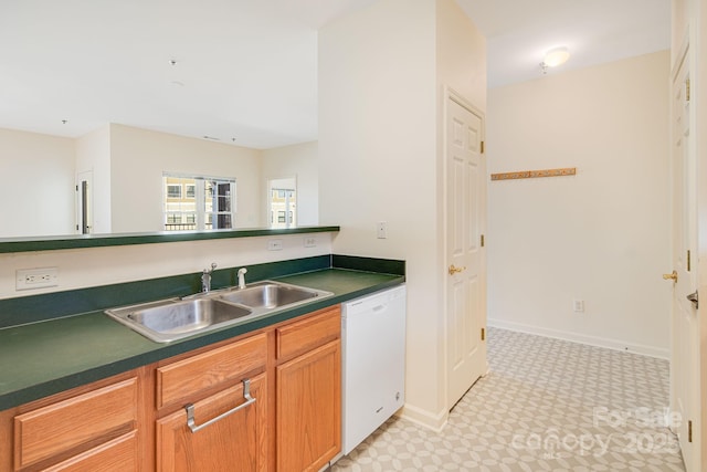 kitchen with dark countertops, white dishwasher, a sink, and baseboards