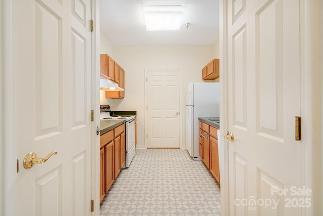 kitchen with under cabinet range hood, white appliances, light floors, brown cabinetry, and dark countertops