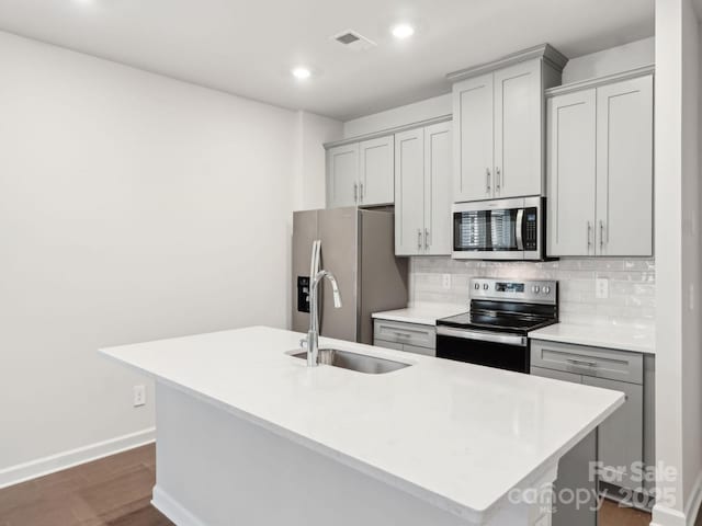 kitchen with gray cabinetry, decorative backsplash, appliances with stainless steel finishes, a kitchen island with sink, and a sink