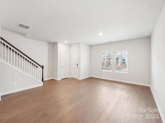 empty room featuring recessed lighting, wood finished floors, visible vents, baseboards, and stairs