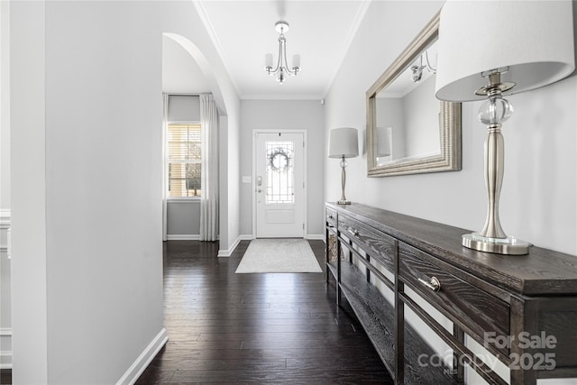 foyer entrance featuring a chandelier, ornamental molding, dark wood-type flooring, and baseboards