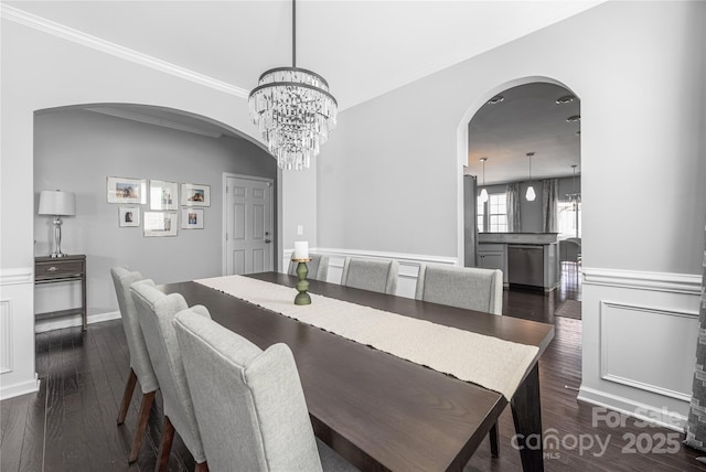 dining area with crown molding, arched walkways, wainscoting, and dark wood finished floors