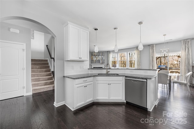 kitchen featuring a peninsula, stainless steel dishwasher, dark stone countertops, and a sink