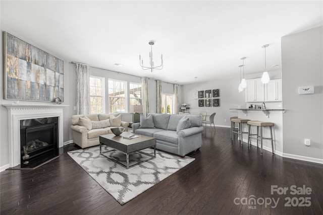 living area with dark wood-style floors, baseboards, a fireplace with raised hearth, and a notable chandelier