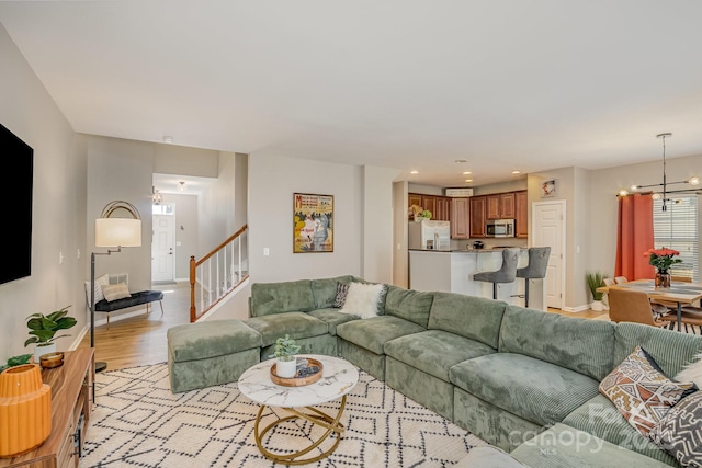 living area with light wood-style floors, stairs, baseboards, and an inviting chandelier