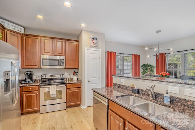 kitchen featuring appliances with stainless steel finishes, brown cabinetry, a sink, and light wood-style floors