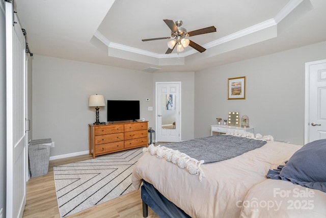 bedroom featuring a tray ceiling, crown molding, ceiling fan, light wood-type flooring, and baseboards