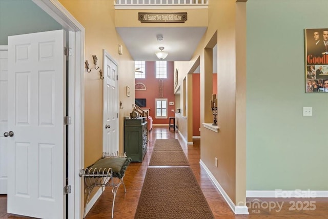 corridor featuring a high ceiling, baseboards, and wood finished floors