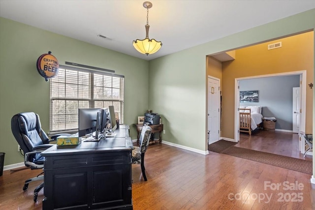 home office with wood finished floors, visible vents, and baseboards