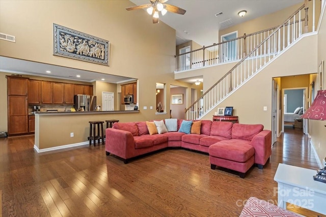 living room featuring stairway, visible vents, a high ceiling, dark wood-style flooring, and ceiling fan