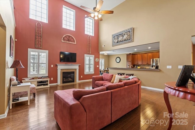 living area featuring baseboards, wood-type flooring, a glass covered fireplace, and a ceiling fan