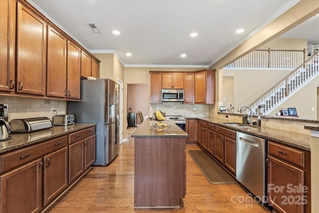 kitchen with dark stone countertops, a sink, light wood-style floors, appliances with stainless steel finishes, and a center island