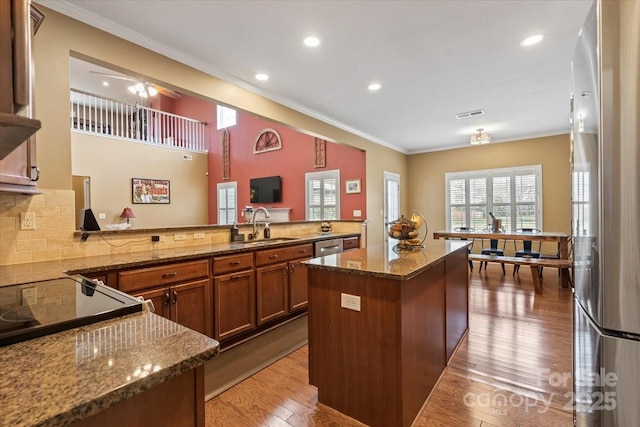 kitchen featuring dark stone counters, light wood-style flooring, a peninsula, brown cabinetry, and stainless steel appliances