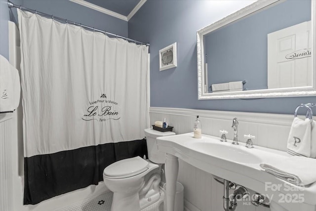 full bath featuring a shower with shower curtain, toilet, wainscoting, and crown molding