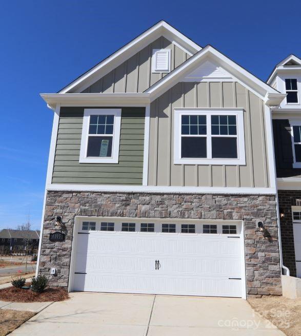 view of side of home featuring a garage, stone siding, board and batten siding, and concrete driveway