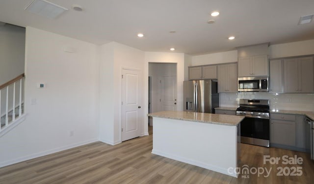 kitchen featuring wood finished floors, a kitchen island, gray cabinets, appliances with stainless steel finishes, and backsplash