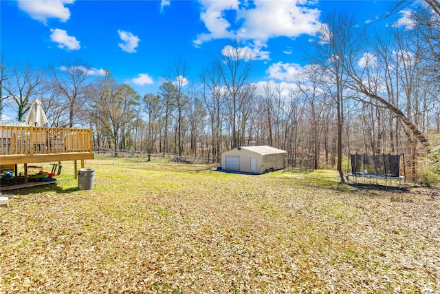 view of yard featuring a trampoline, an outbuilding, a detached garage, fence, and a wooden deck