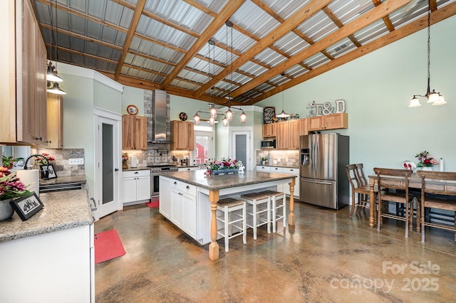 kitchen with decorative light fixtures, appliances with stainless steel finishes, white cabinets, a kitchen island, and wall chimney range hood