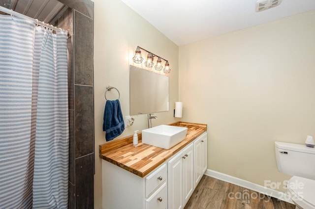 bathroom with toilet, wood finished floors, visible vents, vanity, and baseboards