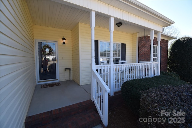 entrance to property featuring a porch and brick siding