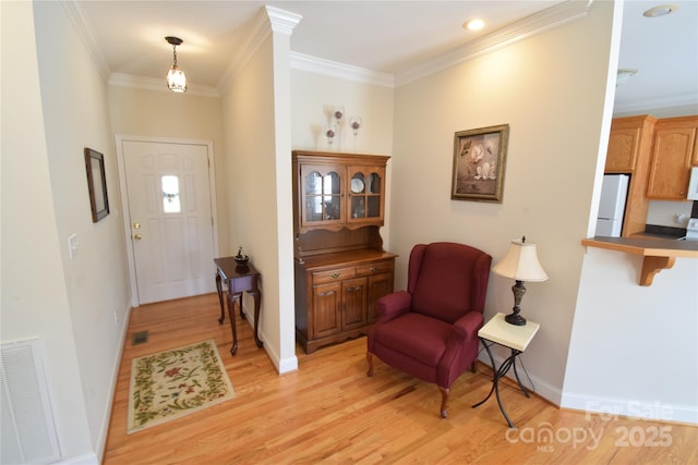 foyer entrance featuring baseboards, light wood finished floors, visible vents, and crown molding